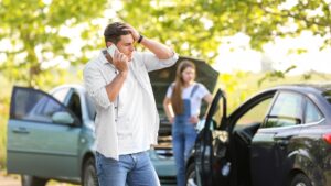 a stressed man on the phone with an auto collision in the background